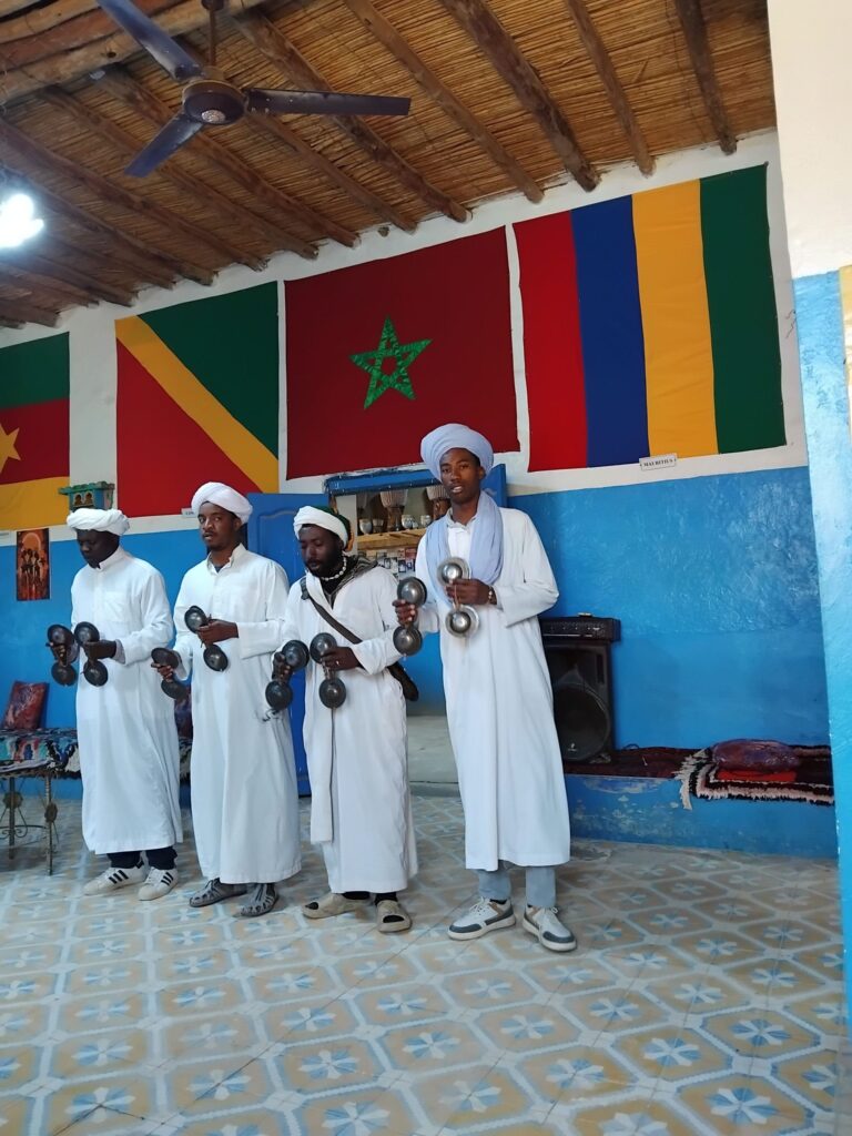 4 men in white robes performing musical act inside, with flag displayed behind them