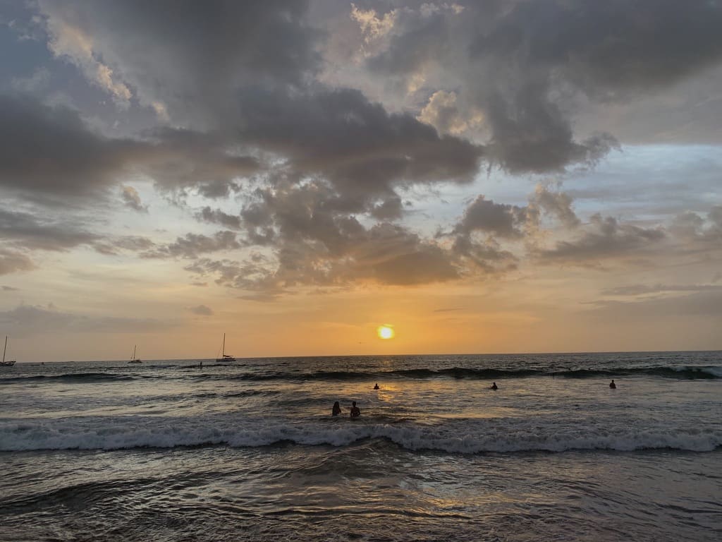 Sunset over a beach with a few swimmers