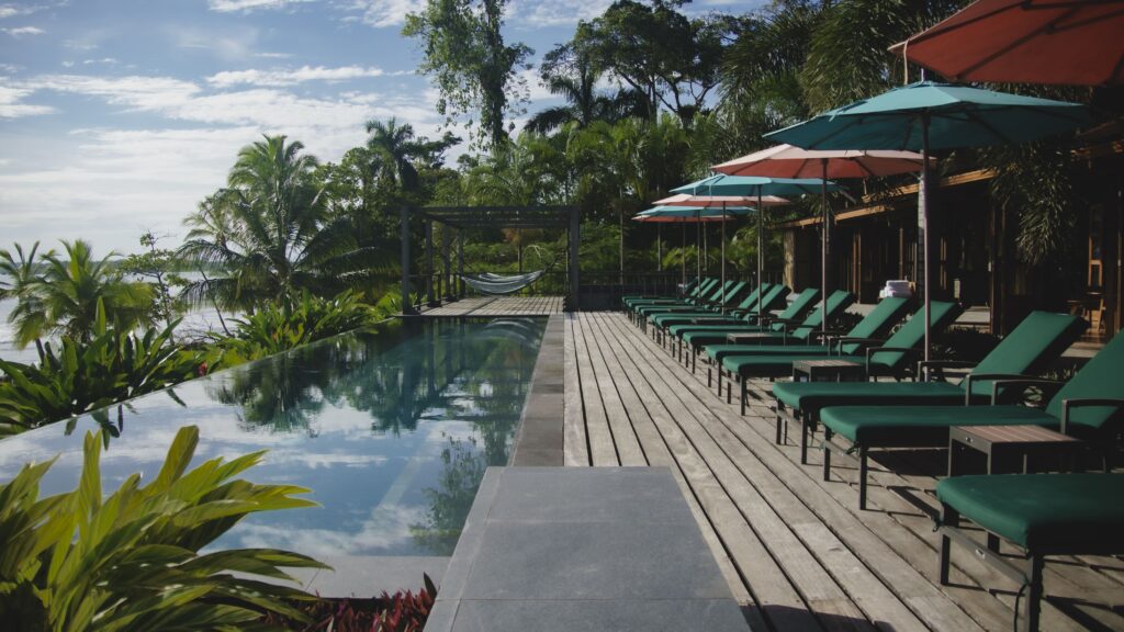 Infinity pool with ocean view in jungle setting with lined up green pool chairs