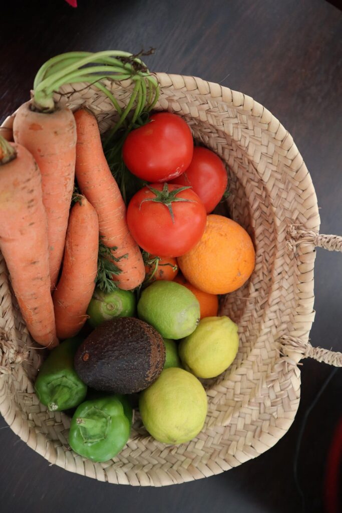 A basket with carrots, tomatoes, lemons, green peppers, and an avocado