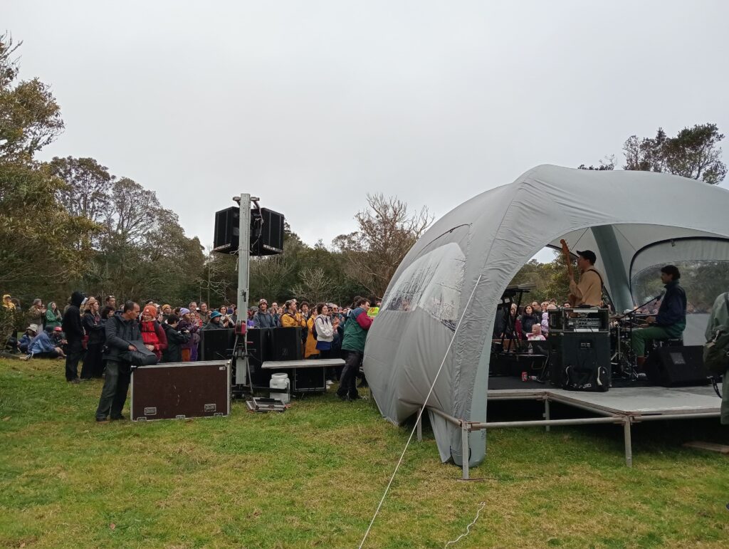 Tent with performers on grass with crowd watching on