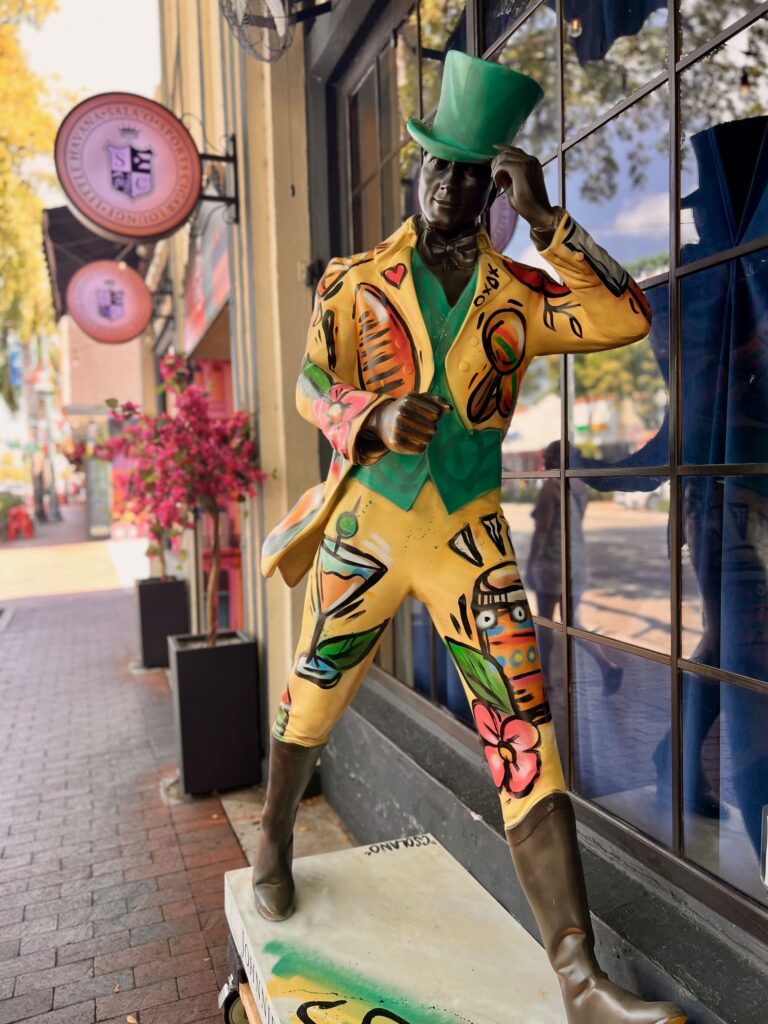 Statue of man in high hat painted in yellow and green, standing outside a shop