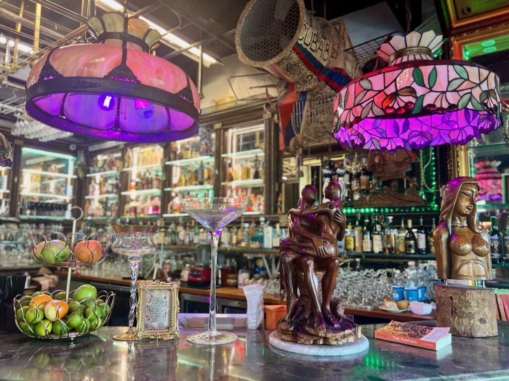 Two purple ceiling lamps lighting up a bar area with status, limes and glasses on the bar