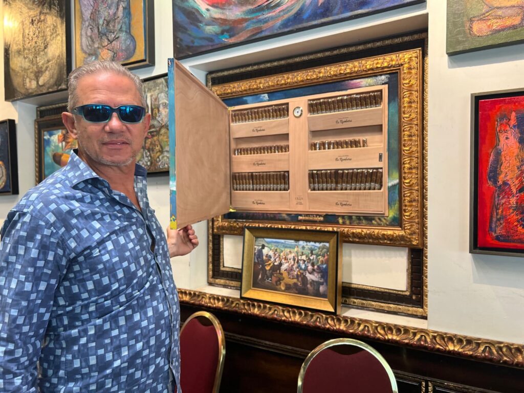 Man in sunglasses opening a display of cuban cigars in an art gallery