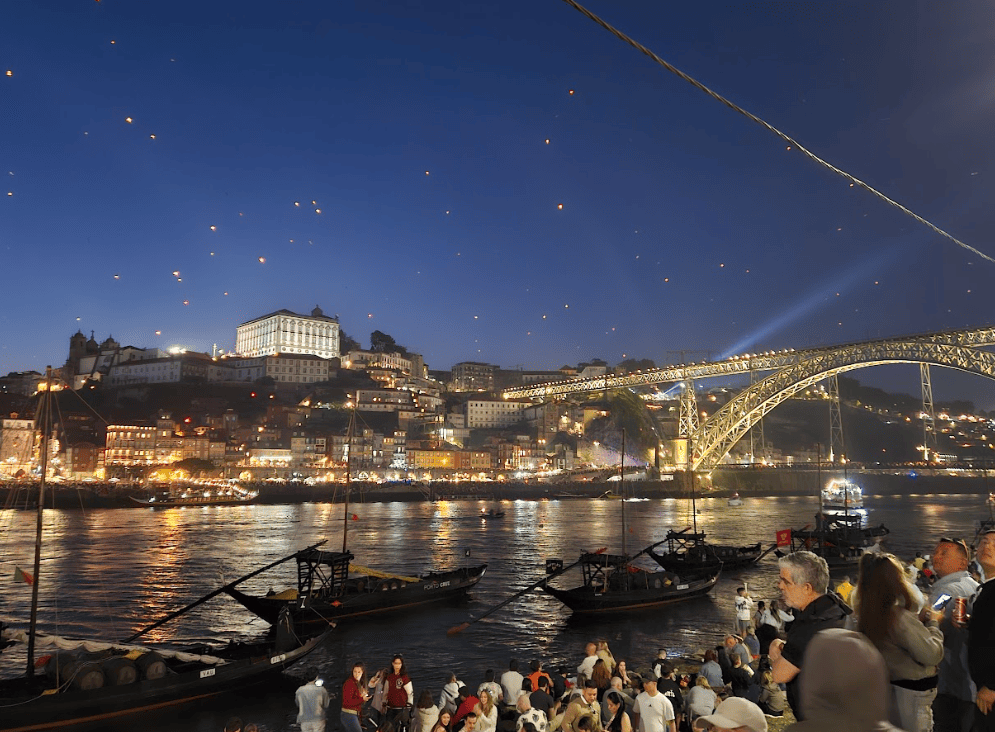 Crowds watching lantern and fireworks from riverside with a lit bridge in the middle