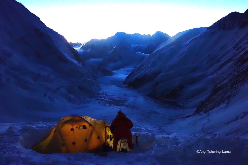 Man sitting next to a lit tent in glacier territory