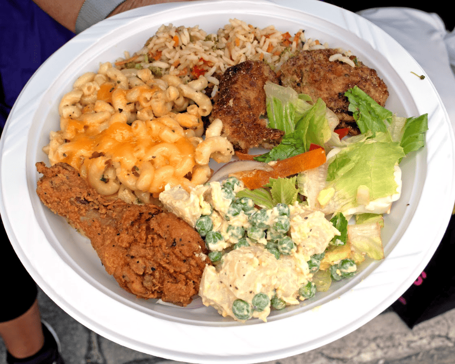 Paper plate with chicken, mac n cheese, salad and rice