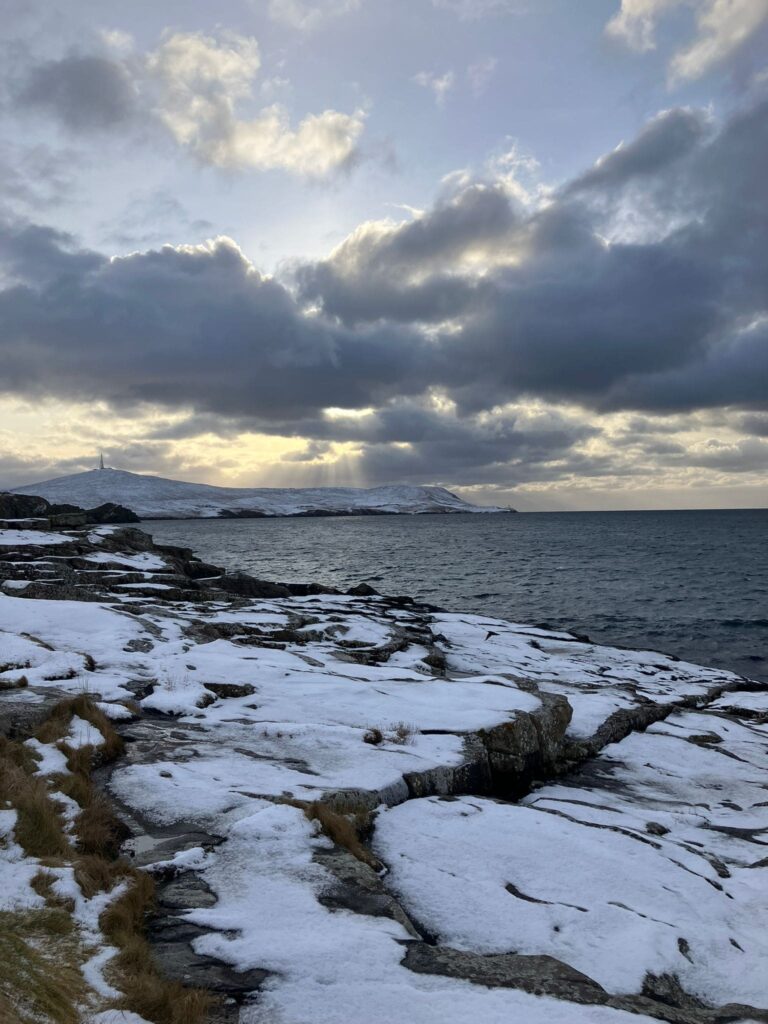 Light from the sky hitting snow covered cliffs by the water