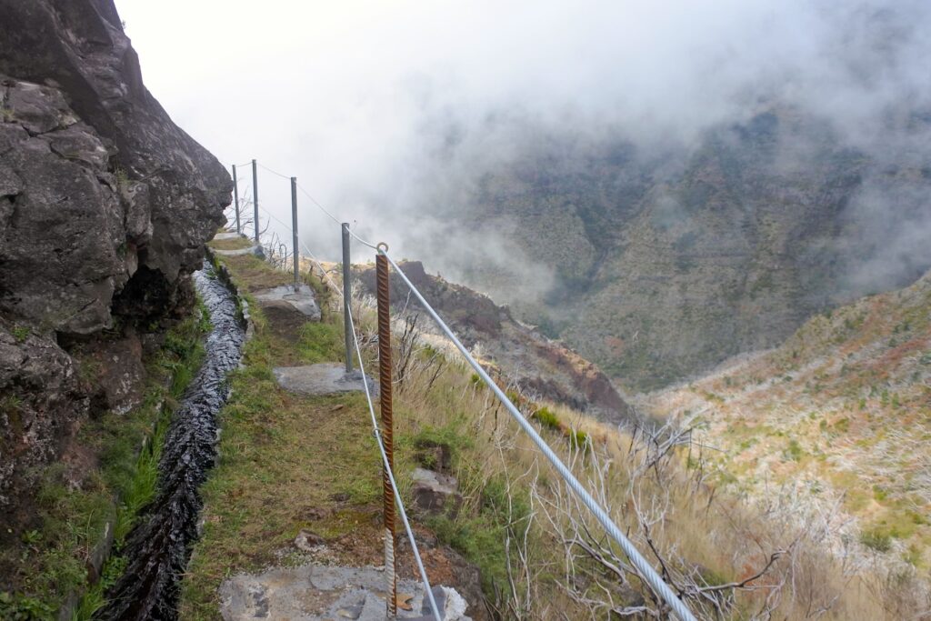 Hiking path with fence near the edge and a small man-made  water stream running alongside the trail