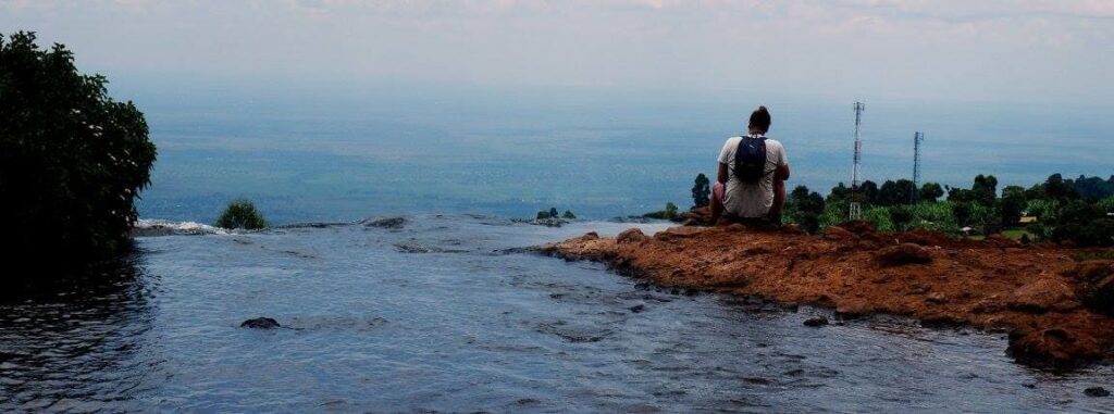 Man sitting on edge of river enjoying view of land below.