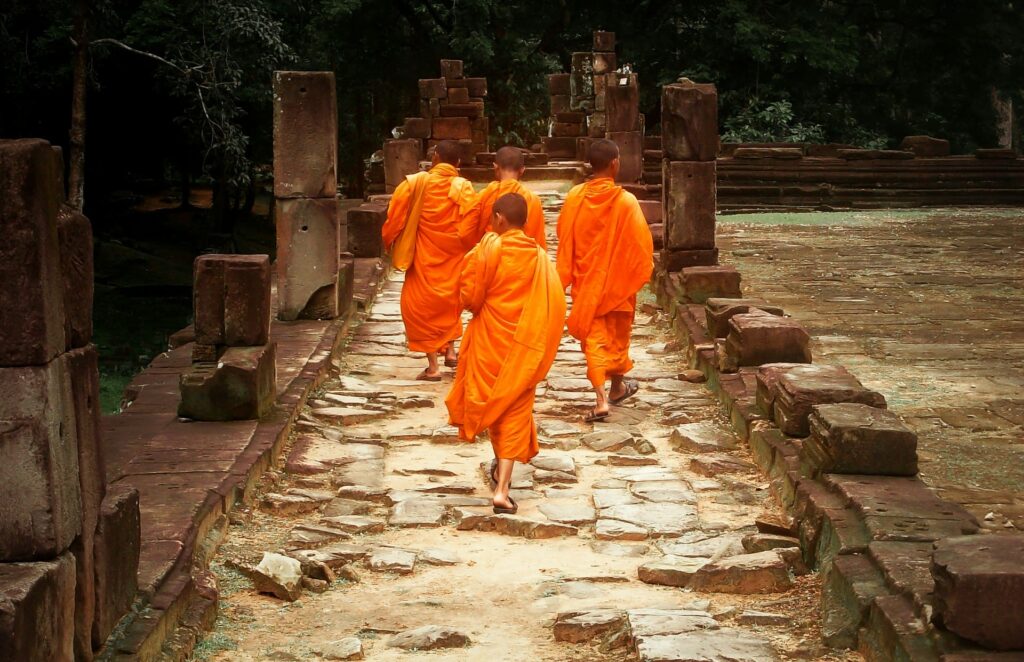 4 monks dressed in orange walking over temple ruins