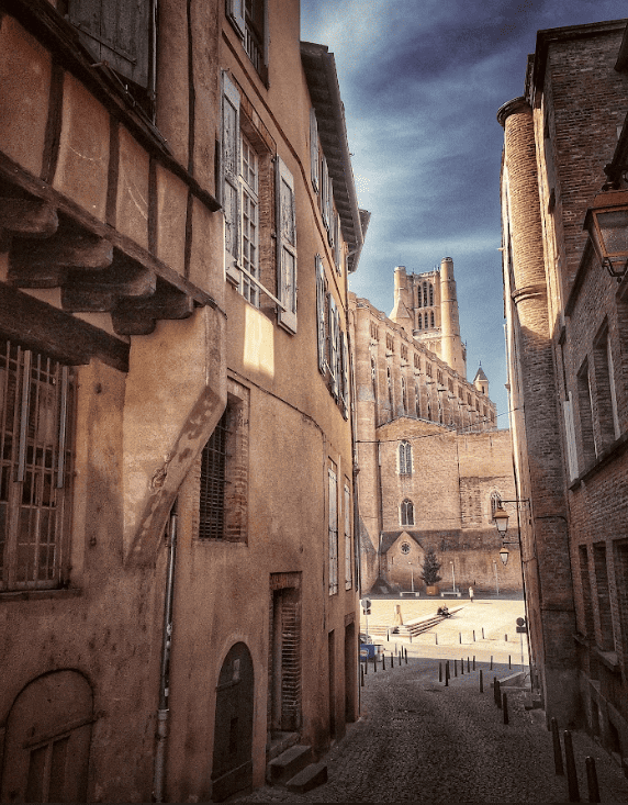 Narrow street between stone facade buildings leading out onto a square and a church