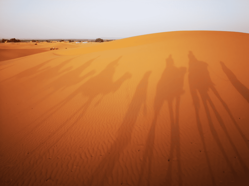 Shadows of people riding camels reflected on sand dunes