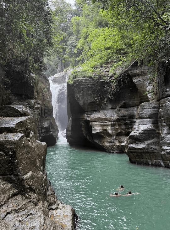 Waterfall amid cliffs with three people swimming in the lake