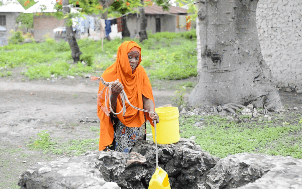 A woman pulling up water from a well with a rope and yellow plastic container