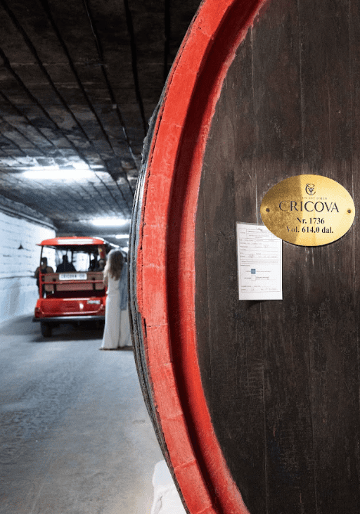 Wine barrel in underground tunnel with red transport vehicle next to it.
