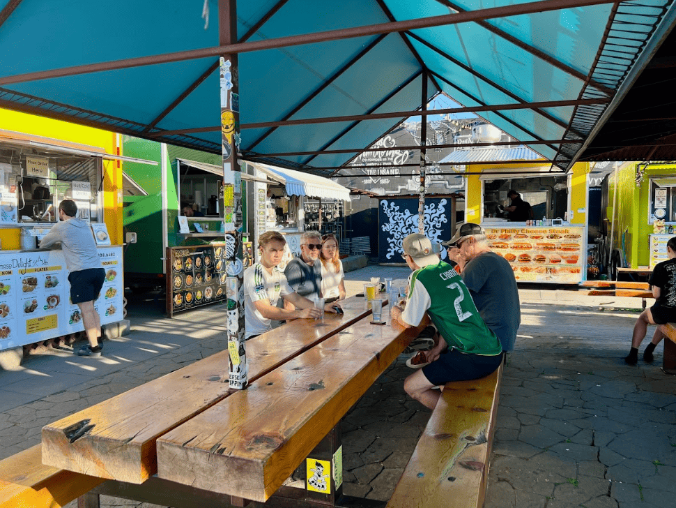 Group of people sitting at shared outdoor table surrounded by food carts